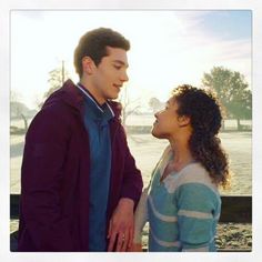 a man and woman standing next to each other in front of a lake with snow on the ground