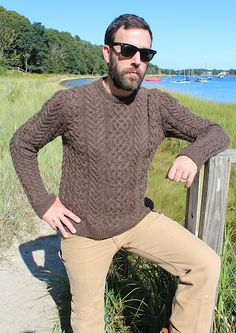 a man wearing sunglasses leaning on a fence near the water with his hands on his hips