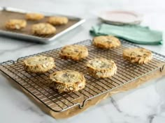 cookies cooling on a wire rack next to a cookie sheet and baking pan with more cookies in the background