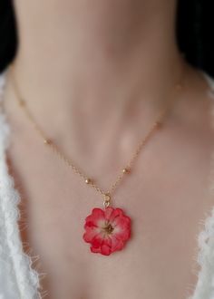 This stunning necklace features a beautiful, pressed red rose flower encased in a clear resin pendant.  The pendant is suspended from a luxurious chain, giving the necklace a touch of elegance and sophistication.  The vibrant red rose flower is a symbol of love and passion, making this necklace the perfect gift for a loved one or a special treat for yourself.  The delicate flower is carefully preserved, ensuring that their natural beauty will last for years to come. The gold-plated chain adds a Preserved Flower Jewelry, Red Flower Pendant Necklace As Gift, Red Flower Pendant Jewelry With Flower Charm, Red Flower Pendant Jewelry With Charm, Red Flower Charm Necklace As A Gift, Red Flower Necklaces For Gifts, Red Flower Necklace With Charm As Gift, Red Flower Charm Necklace For Gift, Dainty Red Flower Pendant Necklace