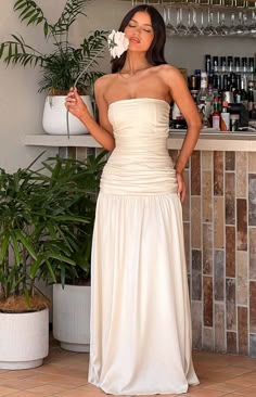 a woman standing in front of a bar wearing a white dress and holding a flower