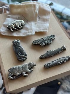 several different metal pins sitting on top of a wooden table next to a white cloth