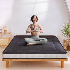 a woman is sitting in the middle of a yoga pose on a mattress with her hands together