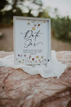 a sign that is sitting on top of a rock with white flowers and greenery