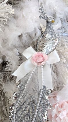 a white and silver christmas tree decorated with feathers, flowers and a bird ornament