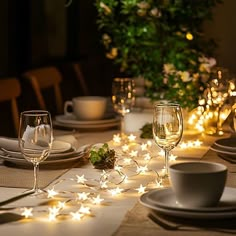 the table is set with white dishes and silverware, lit up by fairy lights