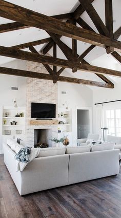 a living room with white couches and wooden beams on the ceiling, along with a fireplace