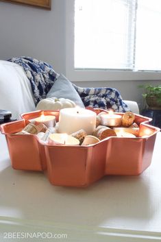 a candle is sitting in an orange pan on a table next to a white couch