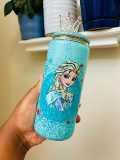 a hand holding a blue glittered cup with a princess on it