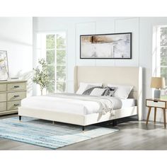 a white bed sitting on top of a wooden floor next to a dresser and mirror