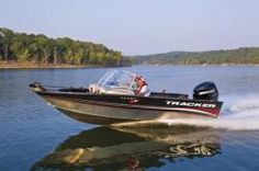 a man driving a speed boat across a lake with trees in the backgroud