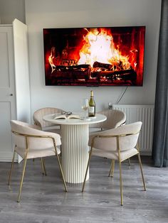 a dining room table and chairs with a painting on the wall above it that has a fire in the fireplace