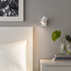 a bed with white sheets and pillows next to a green plant in a glass vase