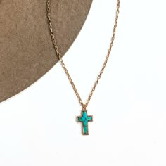 This is a thin gold tone chain necklace with a small cross pendant in the center. The  pendant has a turqouise stone shaped as a cross, the stone is in a gold setting. This  necklace is laying on a white background and on a light brown felt hat brim. Spiritual Cross Turquoise Necklace For Gift, Turquoise Cross Pendant Necklace As Gift, Spiritual Turquoise Necklace With Cross Pendant Gift, Adjustable Turquoise Cross Jewelry, Turquoise Cross Pendant Necklace For Gift, Adjustable Blue Cross Necklace, Blue Adjustable Cross Necklace, Handmade Turquoise Cross Necklace, Handmade Turquoise Cross Pendant Necklace