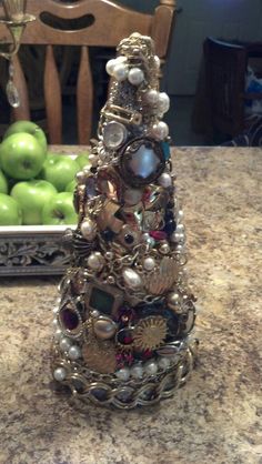 a christmas tree made out of jewelry sits on a kitchen counter next to green apples