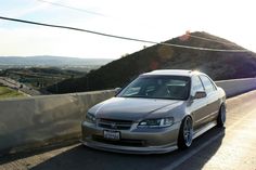 a silver car parked on the side of a mountain road near a highway with mountains in the background