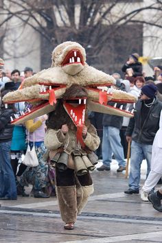 a man in costume walking down the street with an animal mask on his head and other people behind him