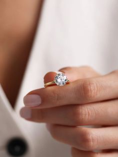 a woman's hand holding a ring with a diamond on it and the middle finger