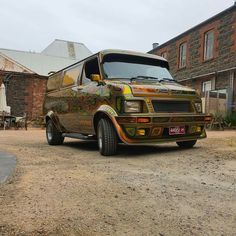 an old van painted with colorful designs parked in front of a brick building on a dirt road