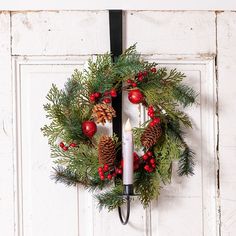 a christmas wreath hanging on a door with a lit candle and pine cones in the center