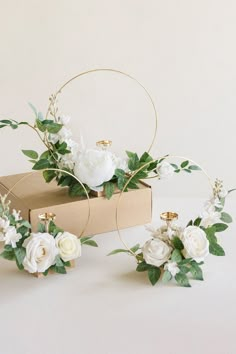 white flowers and greenery are arranged in gold hoop vases on top of a cardboard box