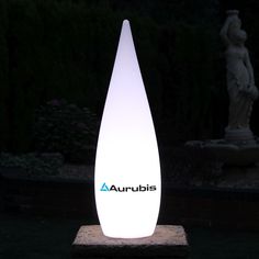 an illuminated vase sitting on top of a stone block in front of a garden statue