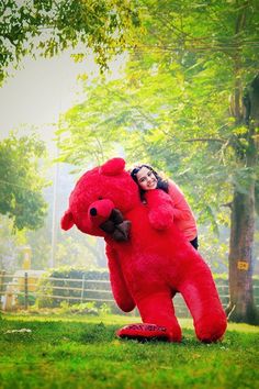 a woman is hugging a giant red teddy bear in the middle of a grassy area