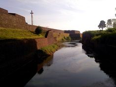 a river running through a lush green field next to a brick wall and grass covered hillside