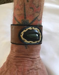 This is a unique handcrafted brown leather cuff with a good size jade nugget in a nice bezel setting (waxed threat) . The edges of the leather cuff are tooled, edged and stained..the cuff has 2 snaps for adjustment....the length of the wristband is 9 inches and fits a 7 or 6 inch wrist...the width is 1 1/2 inches the leather is a nice thick brown latigo and the snaps are copper. Leather Concho Cuff Bracelet, Leather Cuff Bracelet With Concho, Brown Leather Cuff Jewelry, Hand Wrapped Brown Leather Jewelry, Artisan Brown Concho Cuff Bracelet, Artisan Brown Cuff Bracelet With Concho, Brown Leather Bracelet With Concho, Artisan Hand Wrapped Leather Bracelet, Artisan Hand-wrapped Leather Bracelet