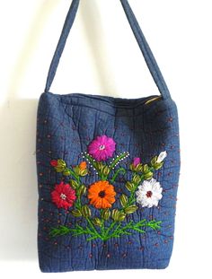 a blue purse with flowers on it hanging from a hook in a wall next to a white wall