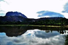 a lake with mountains in the background and clouds reflecting on it's water surface