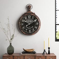 a clock on the wall above a dresser with candles and vases next to it