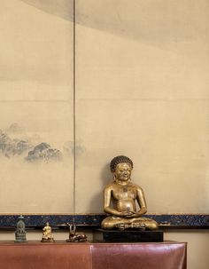 a buddha statue sitting on top of a wooden table next to a brown leather chair