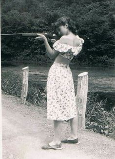 an old black and white photo of a woman in a dress holding a baseball bat