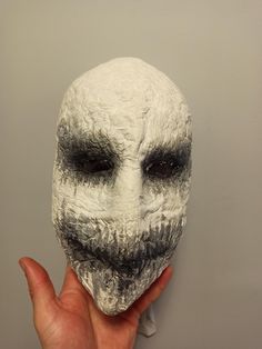 a person holding up a white mask with black and grey hair on it's face