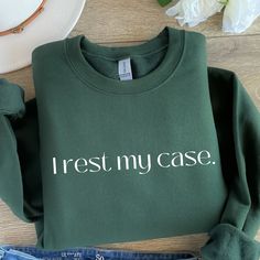 a green sweatshirt with the words i rest my case printed on it next to jeans