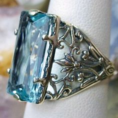 Sky Blue Aquamarine Ring Baguette Design#32 Introducing the Baguette D32, a stunning piece of wearable art that pays homage to the opulent Victorian era. Crafted with meticulous attention to detail, this exquisite filigree Antique reproduction in sterling silver is sure to captivate anyone with a love for vintage-inspired jewelry. At its center, lies a flawless 7ct sky blue gemstone, radiating a dazzling hue that catches the light with every movement. The baguette rectangle-cut gemstone measures Blue Rectangular Jewelry For Party, Rectangular Light Blue Jewelry Gift, Elegant Turquoise Jewelry With Rectangular Stone, Elegant Turquoise Rectangular Stone Jewelry, Exquisite Blue Jewelry With Intricate Design, Elegant Engraved Blue Jewelry, Formal Turquoise Rectangular Jewelry, Rectangular Aquamarine Jewelry For Wedding, Elegant Aquamarine Rectangular Jewelry