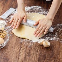 a woman rolling out dough on top of a wooden table