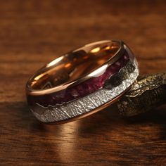 two wedding bands with different colored stones on top of each other, sitting on a wooden surface