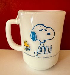 a white coffee cup with a cartoon snoopy on it's side sitting on a table