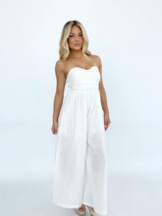 Effortlessly elegant, this versatile jumpsuit is perfect for any summer occasion. The bright and coastal design, featuring a lined and wide leg silhouette, makes it the perfect choice for a wedding, vacation, or resort getaway. The tie detail and strapless design exude luxury and style, while the stretchy smocked back panel ensures both comfort and a flattering fit. With pocket details for added convenience, this jumpsuit is a must-have for your summer wardrobe. Self 100% Cotton Lining 100% Poly Spring Strapless Jumpsuit For Evening, Strapless Jumpsuit For Spring Evening, Bandeau Strapless Jumpsuit For Spring Evening, Spring Evening Bandeau Strapless Jumpsuit, Spring Evening Strapless Bandeau Jumpsuit, Elegant Summer Bandeau Tube Top, Sleeveless Jumpsuits And Rompers For Wedding Guests In Summer, Chic Bandeau Jumpsuits And Rompers For Spring, Sleeveless Jumpsuits And Rompers For Summer Wedding