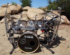 a drum set sitting on top of a dirt field next to rocks and trees in the background