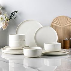 white dishes and cups sitting on top of a table next to a vase with flowers