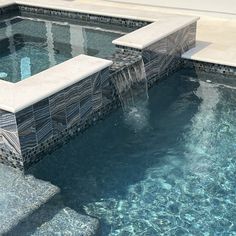 an outdoor swimming pool with water flowing from it's sides and two benches on the side