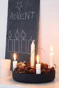 candles and pine cones are arranged in a bowl on a mantle next to a chalkboard