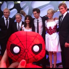 a group of people standing next to each other in front of a spider man stuffed animal