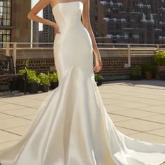 a woman in a white wedding dress standing on a rooftop with her hand on her hip