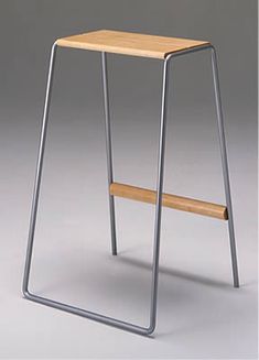 a wooden and metal stool sitting on top of a white floor next to a gray wall