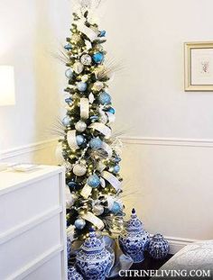 a blue and white christmas tree with ornaments on it in a room next to a bed