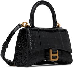 Find BALENCIAGA Hourglass Bag on Editorialist. The Balenciaga Hourglass Bag is crafted from croc-embossed calfskin. It features a rolled carry handle, adjustable and detachable shoulder strap, patch pocket at the back, curved base, logo hardware at the foldover flap, nappa lambskin lining, logo-engraved antiqued gold-tone hardware. The bag measures 5 inches in height, 7.25 inches in width, and 2.5 inches in depth. Balenciaga Hourglass Bag, Hourglass Bag, Baggage Claim, Balenciaga Black, Black Xs, Handle Bag, Travel Luggage, Luggage Bags, Antique Gold